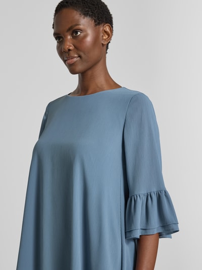 Frauenmodel trägt Relaxed Fit Kleid in Knielänge von Christian Berg Cocktail in Hellblau mit Rüschenbesatz und Halbarm, Nahaufnahme Oberkörper.