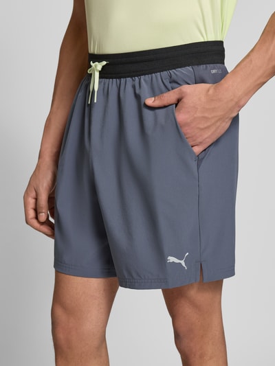 Männermodel trägt Shorts mit elastischem Bund und Logo von PUMA PERFORMANCE aus grauem Material-Mix mit Stretch-Anteil, Nahaufnahme Oberschenkel.
