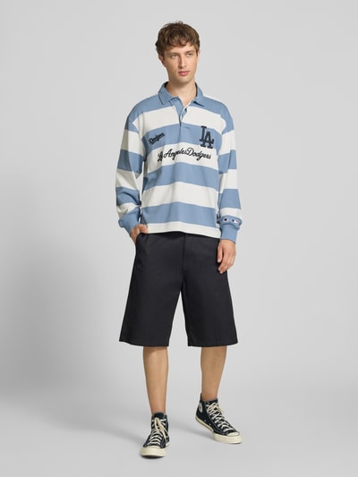 Männermodel trägt Relaxed Fit Poloshirt aus reiner Baumwolle von Champion mit blauen und weißen Streifen sowie Statement-Stitching, Ganzkörperansicht von vorne.