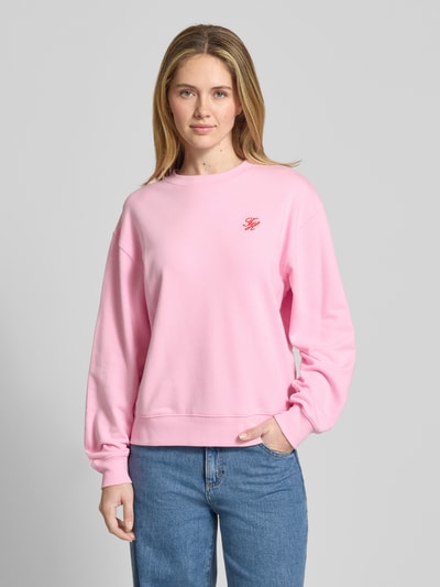 Frauenmodel trägt Regular Fit Sweatshirt aus Baumwoll-Mix von Tommy Hilfiger, Optik: Unifarben, Logo-Detail, Rundhals, Langarm, gerippter Bund und Ärmel, Materialverarbeitung: Sweat, Farbe Rosa, Ganzkörperansicht von vorne.