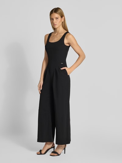 Modelka nosi kombinezon z okrągłym dekoltem Calvin Klein Womenswear, krój regular fit, detal z logo, czarny, długość tyłu w rozmiarze S: 140 cm, szerokość w rozmiarze S: 33 cm, całkowita długość w rozmiarze S: 140 cm, długość wewnętrzna nogawki w rozmiarze S: 74 cm, widok całej sylwetki z przodu.