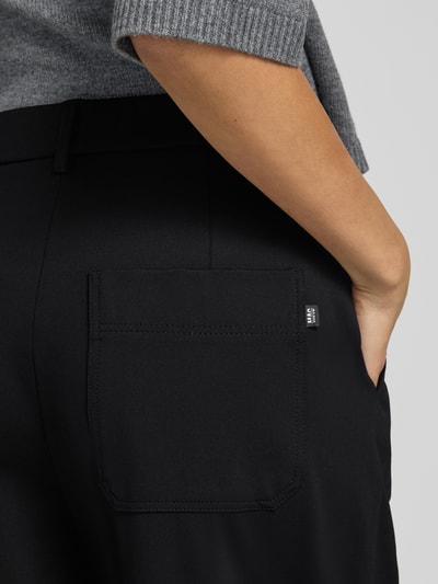 Frauenmodel trägt Regular Fit Hose mit Bundfalten Detail von MAC in Schwarz, sichtbare Gesäßtasche, strukturierte Webware, Nahaufnahme Hüfte, seitliche Perspektive.