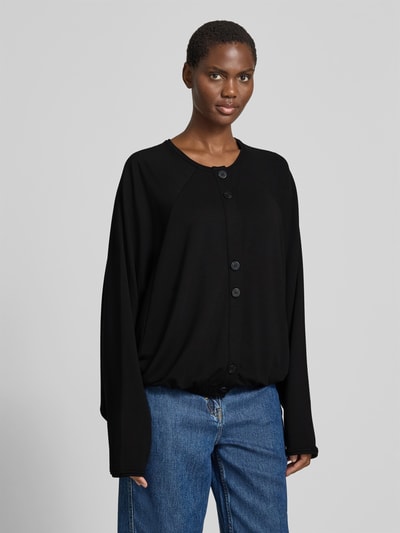 Frauenmodel trägt Oversized Cardigan aus Lyocell-Mix von black palms in Schwarz, mit Rundhalsausschnitt, Knopfleiste, elastische Abschlüsse, Rückenlänge 58 cm bei Größe S/M, Oversized-Fit, Ganzkörperansicht von vorne.