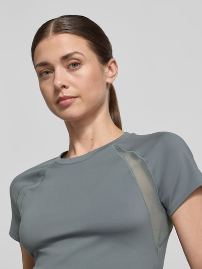 Frauenmodel trägt T-Shirt mit Mesh-Einsätzen und Logo von Under Armour, Damen T-Shirt aus Material-Mix mit Stretch-Anteil, Cropped, Rundhalsausschnitt, Logo, Mesh-Einsätze, Rückenlänge bei Größe S 45 cm, Nahaufnahme Oberkörper.