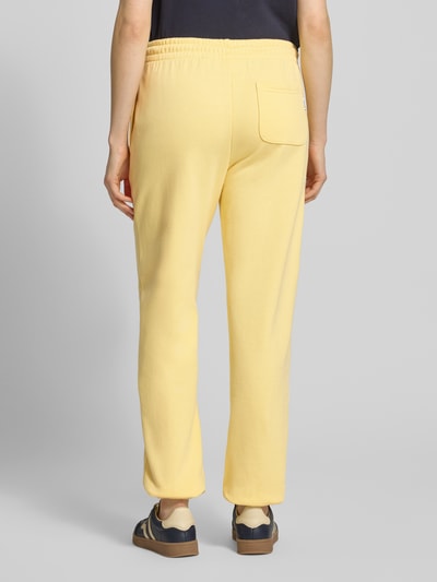 Vrouwenmodel draagt Regular Fit sweatpants met achterzak model 'Nucia' van Mustang in zachtgeel, puur katoen, elastische band met tunnelkoord, steekzakken, elastische zomen, binnenbeenlengte 78 cm, bandwijdte maat S 39 cm, modelnaam op label, pure kleur, gladde textuur. Volledige lichaamsopname achteraanzicht.