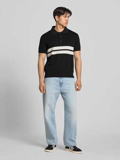 Männermodel trägt Regular Fit Poloshirt aus reiner Baumwolle von Tommy Jeans in Two-Tone-Optik, kurzarm, Strick, Ganzkörperansicht von vorne.