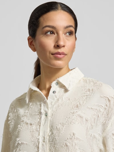 Frauenmodel trägt Boxy Fit Bluse im Allover-Look Modell 'Fenima' von OPUS in Creme, strukturierte Oberfläche, Nahaufnahme Oberkörper.