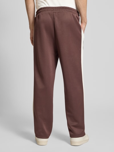 Männermodel trägt Straight Fit Sweatpants mit Logo-Stitching Modell 'Always On' von PUMA PERFORMANCE in Braun mit cremefarbenen Seiteneinsätzen, Material-Mix mit Baumwoll-Anteil, elastischer Bund, Ziernähte und Reißverschlusstaschen, Ganzkörperansicht Rückansicht.