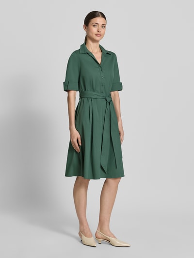 Frauenmodel trägt knielanges Hemdblusenkleid mit Bindegürtel von ROBE LÉGÈRE aus grünem Baumwoll-Mix mit Stretch-Anteil, Taillierter Schnitt, Hemdblusenkragen, kurze Knopfleiste, Ärmel mit Aufschlag, Rückenlänge 104 cm, Brustweite 42 cm, Ärmellänge 30 cm, Ganzkörperansicht von vorne.