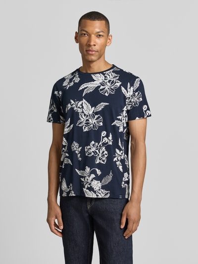 Männermodel trägt T-Shirt mit Rundhalsausschnitt und Label-Detail von Lerros, reine Baumwolle, gerader Schnitt, dunkelblau mit weißem Blumenmuster, Ganzkörperansicht von vorne.