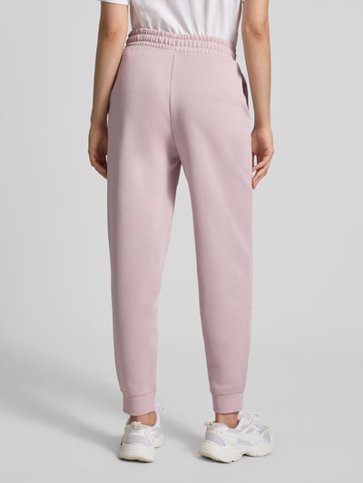 Vrouwenmodel draagt sweatpants met labelstitching en elastische band van PUMA in lichtroze katoenmix, relaxed fit, ganzkörperaanzicht achteraan.