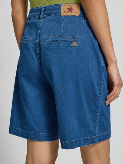 Kobieta nosi szorty chinosy 'Chino Shorts mit Gesäßleistentaschen' od Buena Vista, mieszanka bawełny z dodatkiem streczu, krój wide fit, niebieski, tylne kieszenie z wypustką, szerokość w rozmiarze S 40 cm, długość wewnętrzna nogawki 25 cm, zapięcie na guzik i zamek błyskawiczny, widok całych pleców.