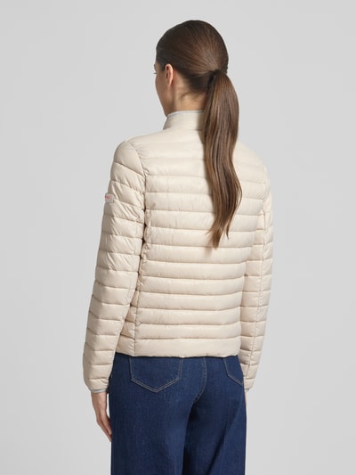 Frauenmodel trägt Steppjacke mit Reißverschlusstaschen Modell 'SISTER JUDY' von Frieda & Freddies, cremefarben, Rückansicht, Ganzkörperansicht. Slim Fit, Stehkragen, sichtbare waagerechte Steppung, glatte Textur. Kontext: Damen Steppjacke, Rückenlänge 56 cm, Schulterbreite 41 cm, Brustweite 47 cm, Ärmellänge 61 cm.