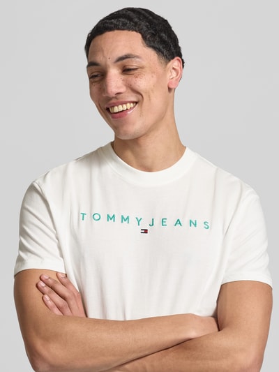 Männermodel trägt Regular Fit T-Shirt aus reiner Baumwolle von Tommy Jeans, unifarben, Rundhals, Label- und Logo-Stitching, Nahaufnahme Oberkörper.