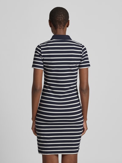 Vrouwenmodel draagt knielanges Polokleid mit kurzer Knopfleiste van Gant, donkerblauw-wit gestreepte katoenmix met stretch, aangesloten fit, polokraag, knielang, korte knoopsluiting, achterkantlengte maat S 88 cm, borstwijdte 42 cm, mouwlengte 19 cm, volledige lichaamsweergave achterkant.