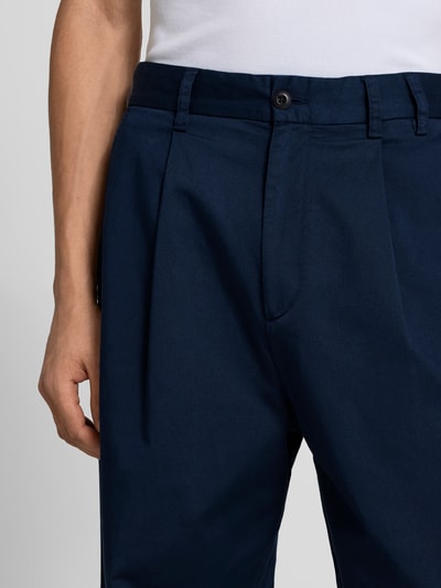 Männermodel trägt Wide Fit Stoffhose mit Bundfalten von Forét in Dunkelblau, elastischer Baumwoll-Mix, Nahaufnahme Oberkörper.
