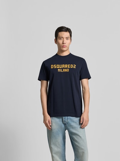 Männermodel trägt Cool Fit T-Shirt aus reiner Baumwolle von Dsquared2, dunkelblau mit gelbem Statement-Print, Ganzkörperansicht von vorne.
