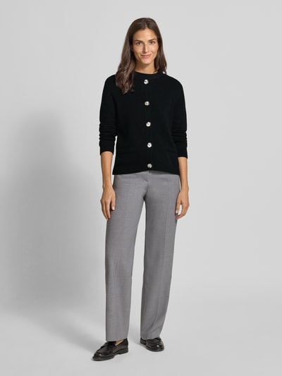 Modelka kobieca ma na sobie Regular Fit Strickjacke mit Viskose- und Kaschmir-Anteil od Milano Italy, czarna, krój regular fit, okrągły dekolt, zapięcie na guziki, kieszenie, elastyczne wykończenia, długość tyłu w rozmiarze S: 51 cm, długość rękawa w rozmiarze S: 63 cm, gładka faktura, całościowy widok z przodu.