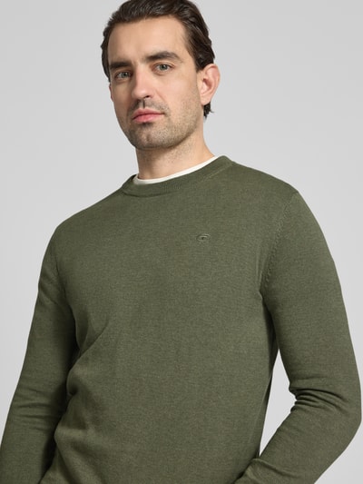 Männermodel trägt Regular Fit Strickpullover aus reiner Baumwolle von Tom Tailor in olivgrün, unifarben, Rundhals, Logo-Detail, Nahaufnahme Oberkörper.