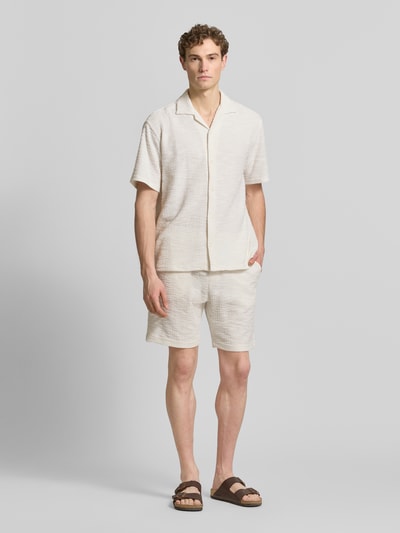Männermodel trägt Regular Fit Freizeithemd mit Strukturmuster von MCNEAL aus Elastischer-Material-Mix mit Baumwoll-Anteil, Kurzärmelig, Reverskragen, durchgehende Knopfleiste, helle Naturtöne, feine Textur, Ganzkörperansicht von vorne.