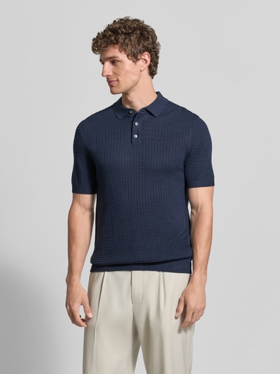 Männermodel trägt Slim Fit Poloshirt in Strick-Optik Modell 'Vanceo' von JOOP! Collection aus reiner Baumwolle, Kurzarm, Ganzkörperansicht von vorne.