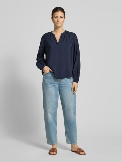 Vrouwenmodel draagt Relaxed Fit Langarmbluse aus Viskose-Mix van s.Oliver RED LABEL in donkerblauw met tuniekhals, omslagnaaddetails, afgeronde rompzoom, lange mouwen met smalle manchet, viscosemix materiaal, Ganzkörperansicht van voren.