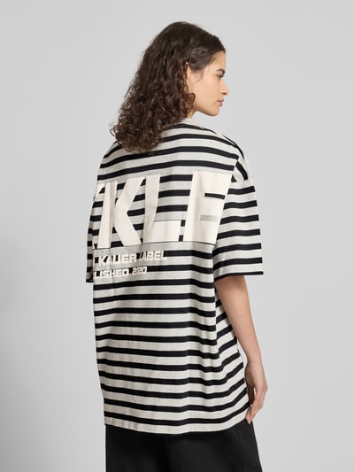 Frauenmodel trägt Oversized T-Shirt mit Label-Print von Karo Kauer, schwarze und weiße Streifen, reine Baumwolle, Rückenansicht, Ganzkörperansicht Rückansicht.