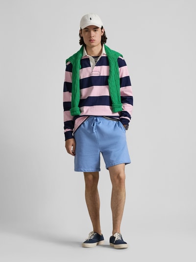 Mężczyzna nosi Regular Fit Sweatshorts aus reiner Baumwolle von Polo Ralph Lauren w kolorze jasnoniebieskim, materiał sweat, logo-stitching, krój regular fit, sznurek w pasie, elastyczny ściągacz, boczne kieszenie, tylna kieszeń, widok całej sylwetki z przodu.