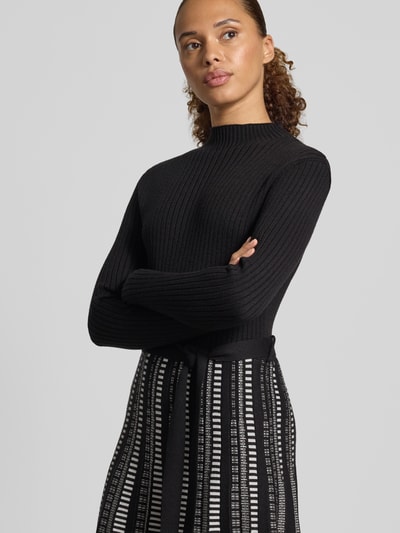 Kobiece modelka ma na sobie sukienkę midi z mieszanki wiskozy od Apricot, imitacja dzianiny, stójka, czarna góra, wzorzysty dół, taliowany krój, długi rękaw, Długość tyłu w rozmiarze S: 108 cm, Szerokość w rozmiarze S: 37 cm, Długość rękawów w rozmiarze S: 61 cm, zbliżenie na górną część ciała z przodu.