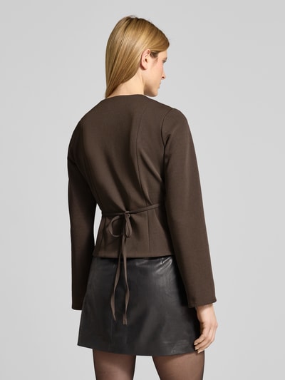 Frauenmodel trägt Blazer mit V-Ausschnitt Modell 'Simmi' von Neo Noir in Braun, Elastischer-Material-Mix, taillierte Passform, Bindeband, Wickel-Optik, Rückenlänge 52 cm, Brustweite 40 cm, Ärmellänge 63 cm, Ganzkörperansicht Rückansicht.