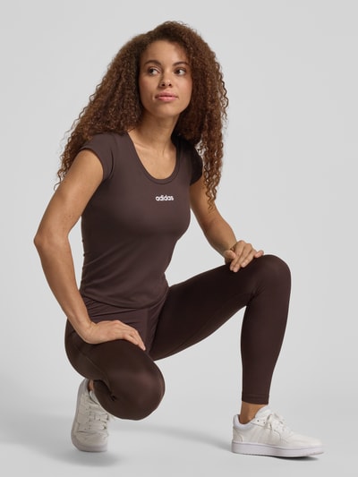 Vrouwenmodel draagt Slim Fit Sport T-Shirt met Label Print van adidas Sportswear in effen bruin, stretchstof, ronde hals, korte mouw, volledige lichaamsaanzicht van voren.
