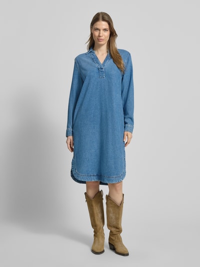Frauenmodel trägt Relaxed Fit Jeanskleid aus Lyocell-Baumwoll-Mix von Marc O'Polo in Denim-Optik mit V-Ausschnitt, Kontrastnähten, Langarm und abgerundetem, geschlitztem Saum, Midi-Länge, seitliche Eingrifftaschen, Ganzkörperansicht von vorne.