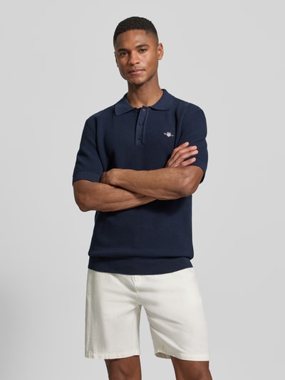 Męski model nosi Regular Fit Poloshirt mit Label-Stitching von Gant z bawełny, kołnierzyk polo, krój regular fit, długość tyłu 68 cm, Ganzkörperansicht von vorne.