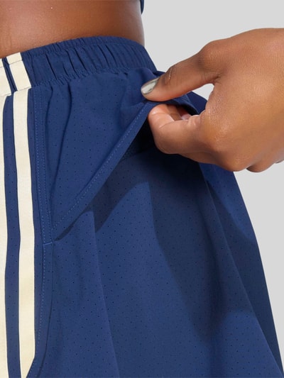Frauenmodel trägt Loose Fit Sportshorts mit Kontraststreifen von adidas Training in Dunkelblau mit beigen Streifen, Detailaufnahme
