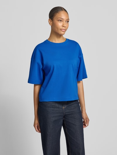 Frauenmodel trägt Oversized T-Shirt aus reiner Baumwolle von s.Oliver RED LABEL in Optik: Unifarben, Passform: Oversized, Logo-Applikation, Rundhals-Ausschnitt, Ärmelform: Kurzarm, Materialverarbeitung: Jersey, Material: reine Baumwolle, kräftiges Blau, glatte Textur, Geradlinige Formen, Ganzkörperansicht von vorne.