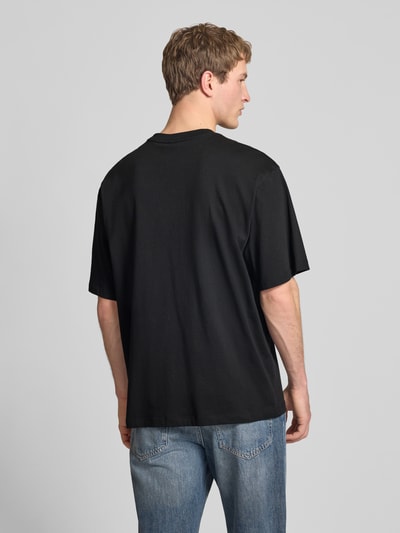 Męski model nosi Oversized T-Shirt mit Logo und Rundhalsausschnitt od The North Face, czarny bawełniany t-shirt, oversize, widok całej sylwetki z tyłu.
