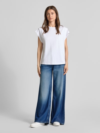 Frauenmodel trägt Wide Leg Jeans im 5-Pocket-Design Modell 'BELLFLOWER' von Guess aus Lyocell-Mix mit Baumwoll-Anteil, ausgestellter Schnitt, mittleres Blau mit sanften Wascheffekten, glatte Textur, Ganzkörperansicht von vorne.
