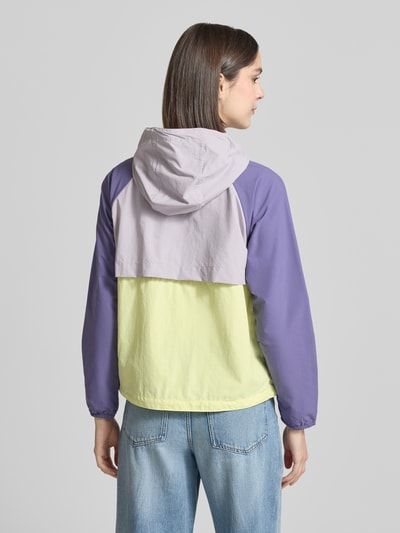 Frauenmodel trägt Windbreaker mit Rückenbelüftungssystem und Kapuze von COLUMBIA in Lila und Gelb mit Logo-Print, Rückenansicht, Ganzkörperansicht Rückansicht. Lockere Passform/Schnitt:, Kapuze mit Kordelzug, Omni-Shield™ Technologie, Wasser- und Schmutzabweisend, Kinnschutz, Rückenbelüftungssystem, Eingrifftaschen mit Reißverschluss, Elastische Bündchen, Saum mit verstellbarem Kordelzug. Rückenlänge bei Größe S: 59 cm, Schulterbreite bei Größe S: 45 cm, Brustweite bei Größe S: 51 cm, Ärmellänge bei Größe S: 57 cm.