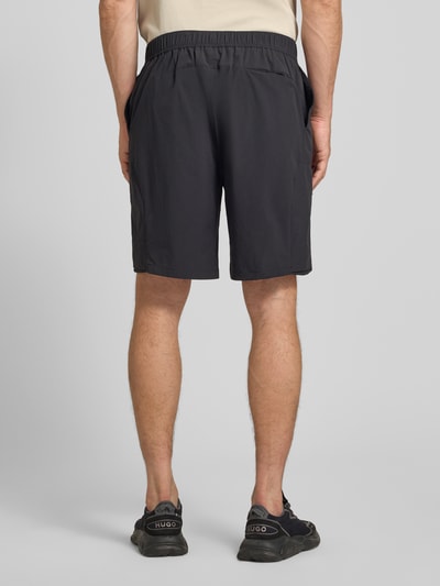 Männermodel trägt Relaxed Fit Cargoshorts mit Label-Schriftzug Modell 'GLOBE CARGO' von BOSS Green in Schwarz, Ganzkörperansicht Rückansicht