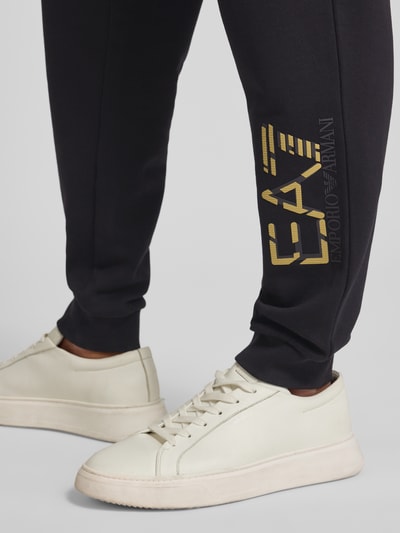 Mężczyzna nosi Spodnie dresowe z elastycznym pasem i nadrukiem z logo od Armani, bawełna, krój regular fit, długość wewnętrzna 78 cm, detaliczny kadr nogawki.