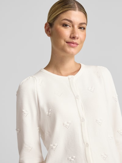 Frauenmodel trägt Strickjacke aus Viskose-Mix Modell 'MANINA' von b.young in Weiß, feine Herzmuster, gerippte Abschlüsse, Nahaufnahme Oberkörper.