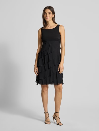 Frauenmodel trägt Knielanges Cocktailkleid mit Volants von Swing, Schwarz, Chiffon, A-Linie, Rundhalsausschnitt, Ganzkörperansicht von vorne.