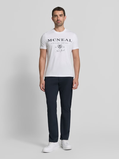 Männermodel trägt Tapered Fit Hose mit Gesäßtaschen von MCNEAL in Dunkelblau, glatte Textur, Eingrifftaschen, Ganzkörperansicht von vorne. Bundweite bei Größe M: 45 cm, Innenbeinlänge bei Größe M: 80 cm, Knopf- und Reißverschluss.