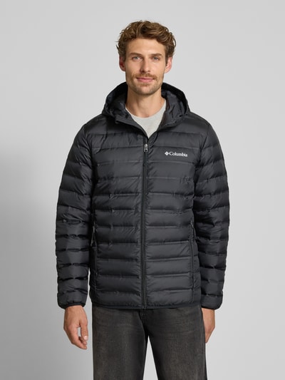 Męski model nosi kurtkę pikowaną Regular Fit Model 'Lake 22™' od Columbia, z efektem pikowania, kaptur, nadruk z logo, zamek błyskawiczny, kolor czarny, długość tyłu w rozmiarze M: 72 cm, szerokość ramion w rozmiarze M: 43 cm, szerokość w rozmiarze M: 42 cm, długość rękawów w rozmiarze M: 70 cm, widok całej sylwetki z przodu.