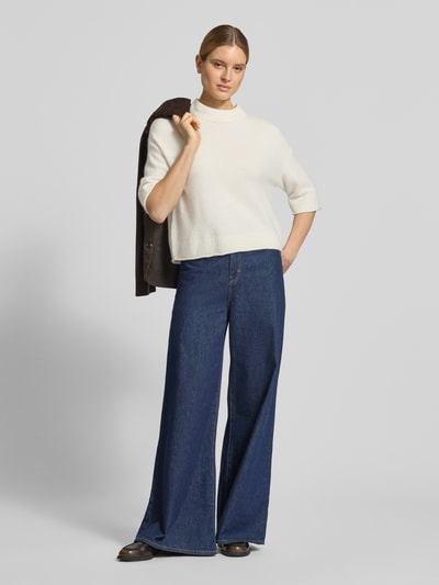 Modelka kobieca nosi Strickshirt mit überschnittenen Schultern Modell 'Pafinna' od OPUS, kremowy kolor, dzianina z moherem, prosty krój, prążkowany dekolt, szerokie rękawy, spodnie jeansowe, tekstura dzianiny, widok całej sylwetki z przodu.