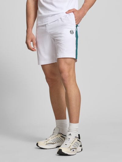 Männermodel trägt Shorts mit Logo-Print Modell 'GOCCIA' von SERGIO TACCHINI aus weißem Material-Mix mit Stretch-Anteil, Lockerer-Schnitt, Ganzkörperansicht von vorne. Bundweite 38 cm, Innenbeinlänge 19 cm, elastischer Bund, auffälliger Logo-Print.