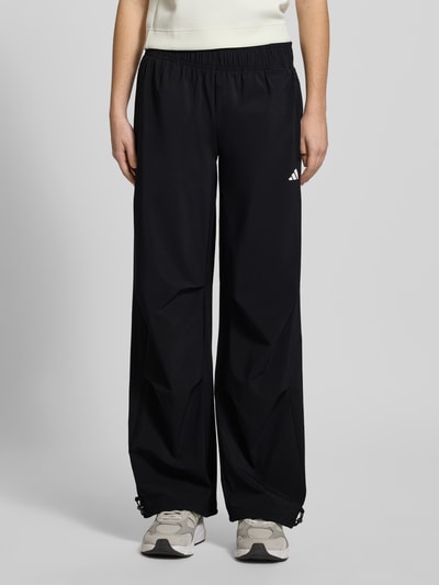 Frauenmodel trägt Wide Fit Stoffhose mit Logo-Print von adidas Sportswear in Schwarz, elastischer Bund, weiter Schnitt, Nahaufnahme Unterkörper.