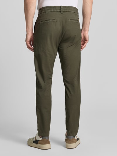 Męski model nosi Tapered Chino aus Baumwoll-Mix Modell 'CHINO-TAPERED-DS-10' od BOSS Orange, oliwkowy, krój tapered, elastyczny pas, kieszenie boczne i z tyłu, bawełniany materiał, gładka faktura, całkowity widok z tyłu.