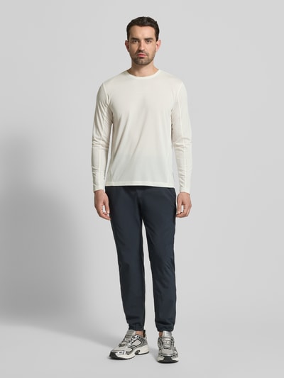 Männermodel trägt Funktionsshirt mit Logo und Rundhalsausschnitt von Salomon in Weiß, kombiniert mit dunkler Hose, Regular Fit, Langarmshirt, Rückenlänge bei Größe M 69 cm, Ganzkörperansicht von vorne.