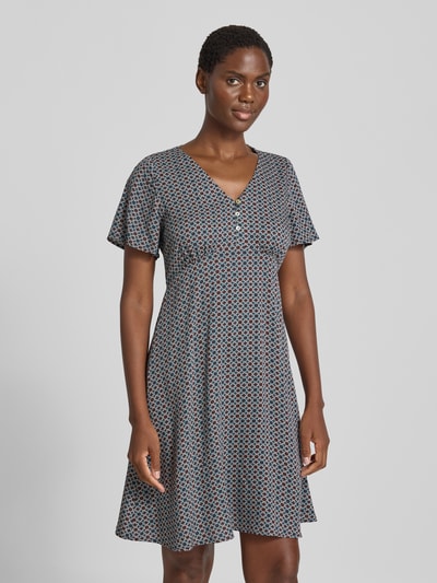 Modelka nosi Knielanges Kleid aus Viskose mit V-Ausschnitt od zero, wzór w drobne geometryczne kształty, taliowany krój, długość do kolan, dekolt w serek, krótka listwa guzikowa, wiązany pasek; Długość tyłu w rozmiarze 36: 90 cm, Szerokość w rozmiarze 36: 32 cm, Długość rękawów w rozmiarze 36: 21 cm. Ganzkörperansicht z przodu